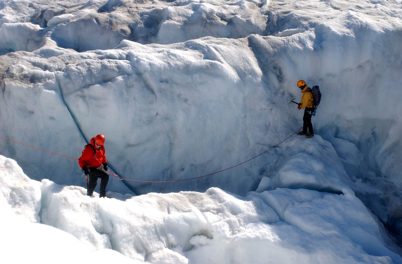 gallery-05 Two climbers navigate a glacier crevasse using ropes and ice axes in winter conditions.