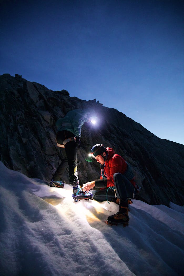 cta-02 Two climbers explore a snowy mountain at dusk, lighting their path.