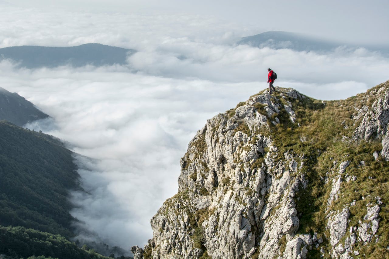 gallery-02 Hiker in red standing on a rocky mountain summit enveloped by clouds.