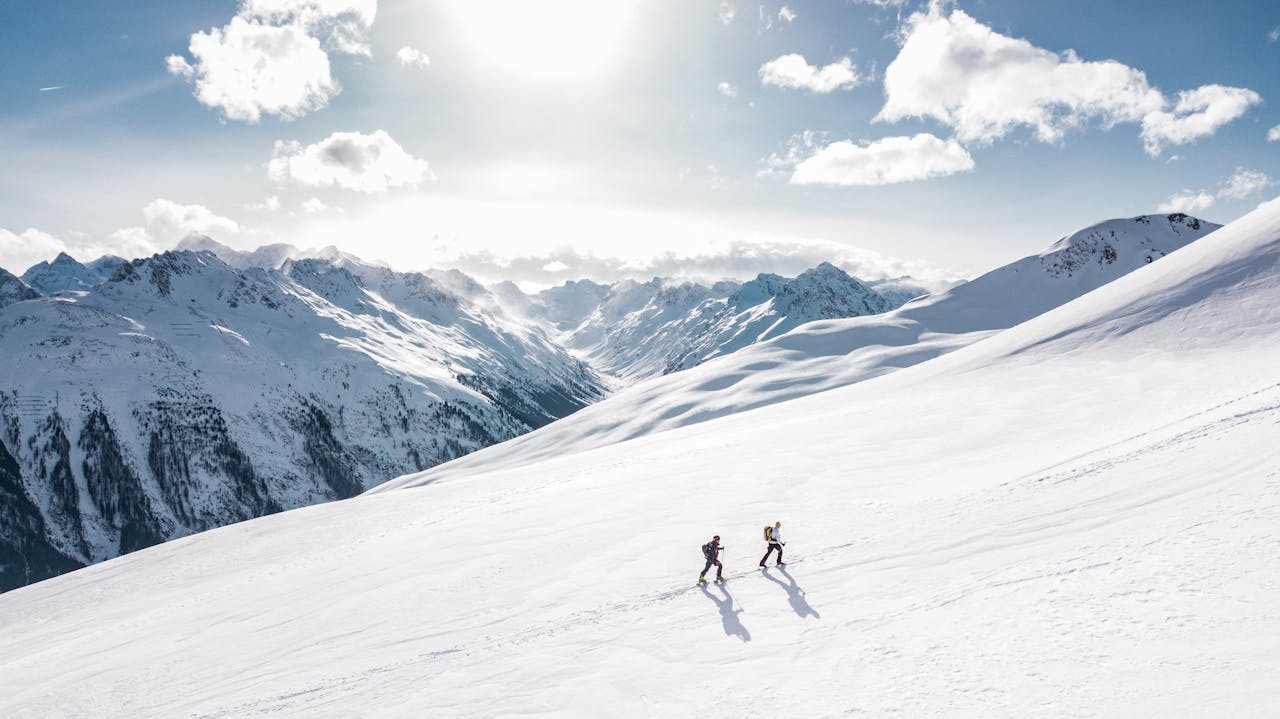 services-01 Two skiers climbing a sunlit snowy mountain slope in Ischgl, Austria, during winter.
